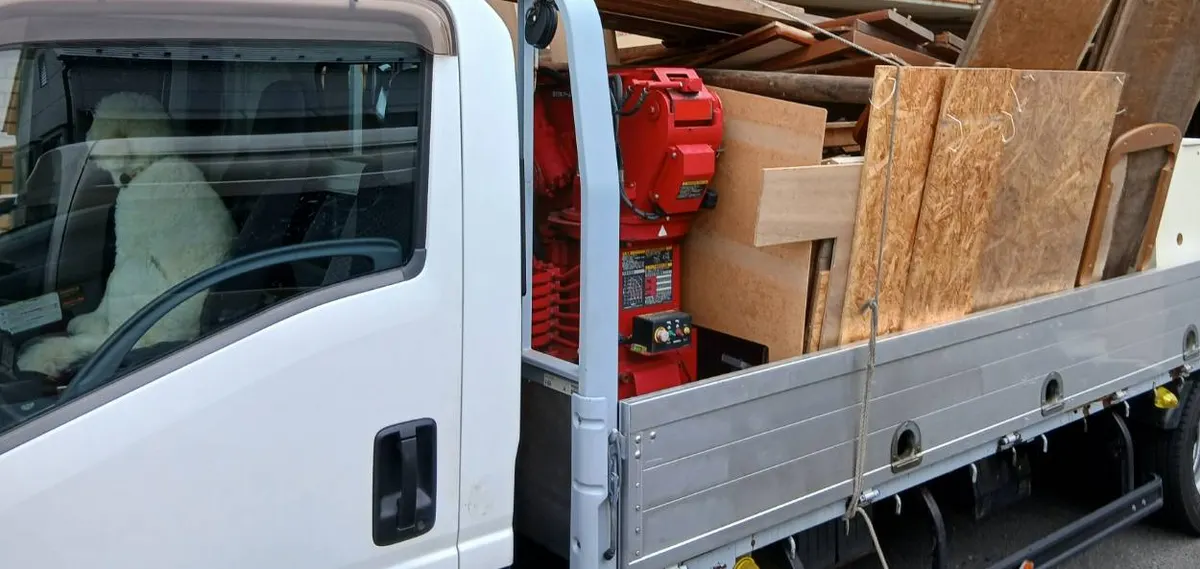 白いトラックの運転席と、板や家具の部材を積んだ荷台。荷台に赤いクレーンが付いている